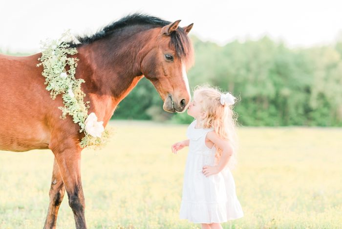 girl kissing pony on the nose wearing a flower garland