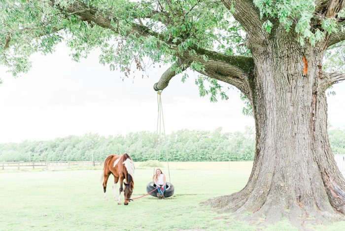 equine photography session capturing a girl on a tire swing as her horse grazes