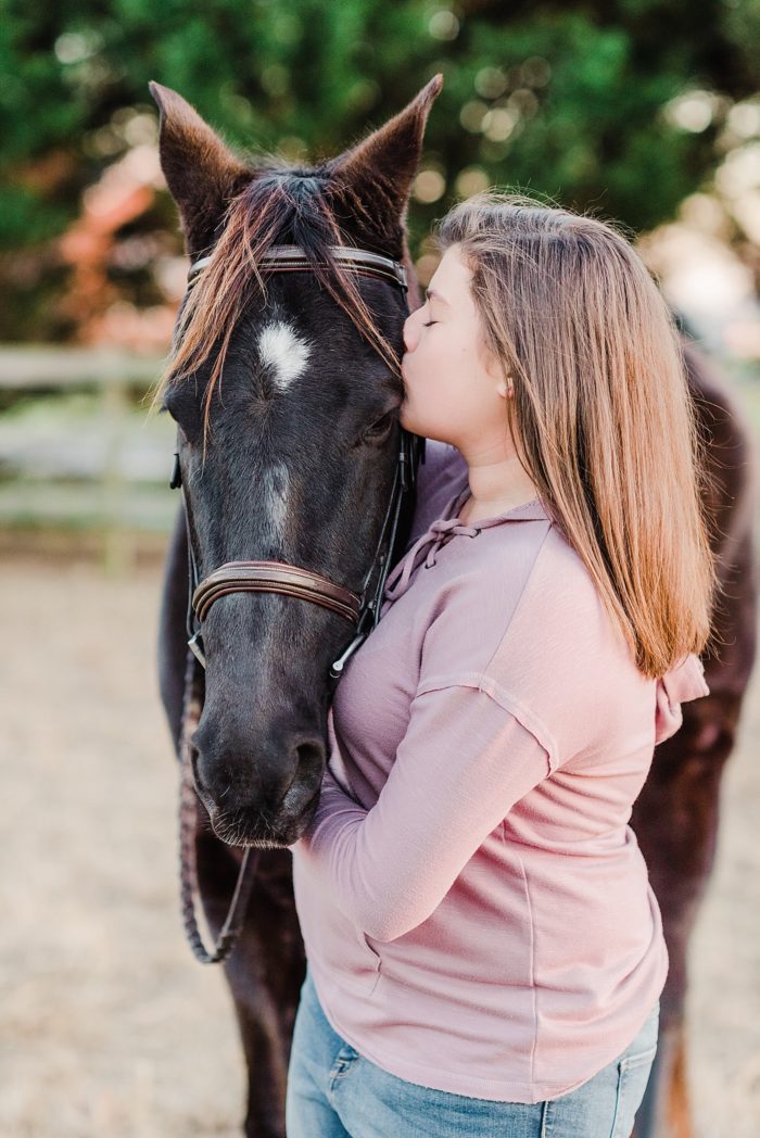 girl kissing black horse on eye